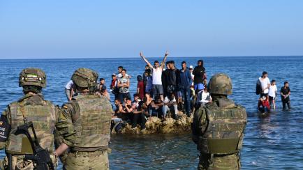 Unos soldados hacen guardia frente a unos jóvenes migrantes subidos a una roca en la playa en Ceuta. 