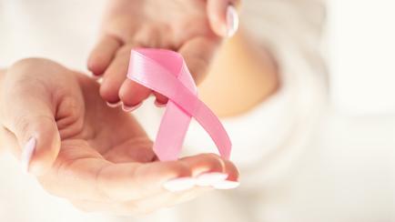 Breast cancer symbol pink ribbon in tender female hands. October health and medicine concept.