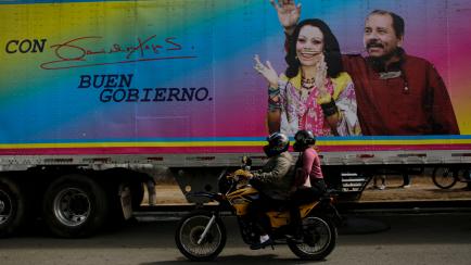 Motocicleta pasando por delante de un cartel electoral en un camión de Daniel Ortega, presidente de Nicaragua y su esposa Rosario Murillo, vicepresidenta.
