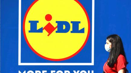 Una mujer con mascarilla pasa por delante de un logo del supermercado Lidl.