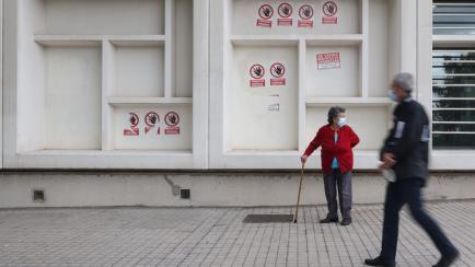 Dos personas mayores en el centro de salud de Pavones (Madrid), donde varios carteles dicen 'Urgencias Cerradas, tu salud vendida', el 21 de octubre de 2022. 