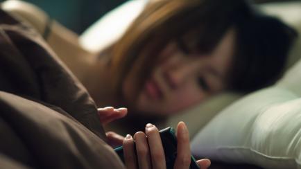 Young woman lying on side in bed operating smartphone