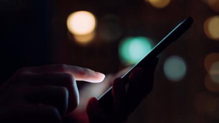 Close up of woman's hand using smartphone in the dark, against illuminated city light bokeh