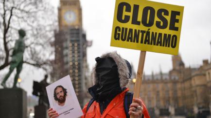 LONDON, UNITED KINGDOM - 2022/01/08: A protester holds a placard and portrait of detainee during the demonstration. 
Amnesty International activists dressed in orange jumpsuits and hoods, representing the 39 men still held in the Guantanamo Bay ...
