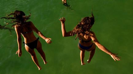 Two women jump from a platform over the water at La Concha beach during a hot summer day in the basque city of San Sebastian, northern Spain, Friday, Aug. 3, 2018. Hot air from Africa is bringing a heat wave to Europe, prompting health warnings ...