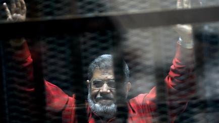 FILE - In this June 21, 2015 file photo, former Egyptian President Mohammed Morsi, wearing a red jumpsuit that designates he has been sentenced to death, raises his hands inside a defendants cage in a makeshift courtroom at the national police a...