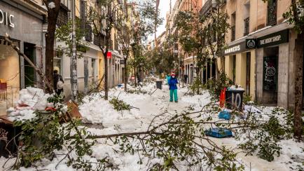 People walk along a street with snow and fallen tree branches during after a heavy snowfall in downtown Madrid, Spain, Sunday, Jan. 10, 2021. A large part of central Spain including the capital of Madrid are slowly clearing snow after the countr...