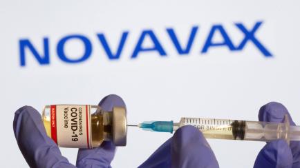 FILE PHOTO: A woman holds a small bottle labeled with a "Coronavirus COVID-19 Vaccine" sticker and a medical syringe in front of displayed Novavax logo in this illustration taken, October 30, 2020. REUTERS/Dado Ruvic/File Photo