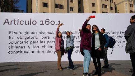 People takes selfies in front of the banner showing Article 160.1 that is part of the proposed, new Constitution in Plaza Italia square in Santiago, Chile, Tuesday, Aug. 23, 2022. The foundation "Pacto Social," or Social Pact, created the urban ...