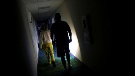 Una pareja camina por el pasillo de un hotel en Florida iluminándose con una linterna. 