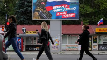 People walk past a billboard displaying a soldier and a Russian flag and reading 'We believe in our army and our victory' in Luhansk, Luhansk People's Republic controlled by Russia-backed separatists, eastern Ukraine, Tuesday, Sept. 27, 2022. Vo...