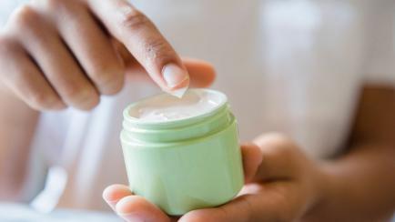 Close up of African American woman dipping finger in lotion jar