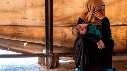 TOPSHOT - A volunteer caretaker who looks after 24 orphaned children, reportedly linked with foreign fighters of the Islamic State (IS) group, covers her face as she carries a child at a camp in the northern Syrian village of Ain Issa, on Septem...