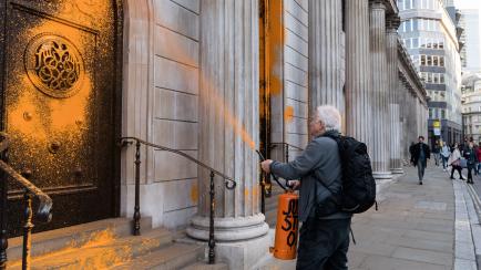 Un miembro del colectivo Just Stop Oil, lanzando pintura naranja contra la fachada del Banco de Inglaterra.