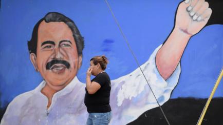 Una mujer camina frente a un mural del presidente de Nicaragua.