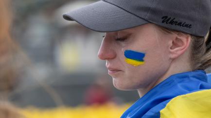 Una mujer, con la bandera ucraniana en la cara y sobre su cuerpo, llora