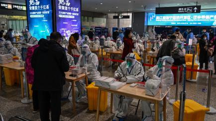 Health workers wait to test passengers for the Covid-19 coronavirus after their arrival at Hongqiao railway station in Shanghai, on December 6, 2022. (Photo by Hector RETAMAL / AFP) (Photo by HECTOR RETAMAL/AFP via Getty Images)