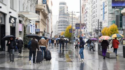 Varias personas caminan con paraguas en la Gran Vía de Madrid. 
