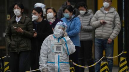 A worker in a protective suit talks on her phone as residents wearing face masks stand in line for their routine COVID-19 tests at a testing site in Beijing, Thursday, Nov. 24, 2022. (AP Photo/Andy Wong)