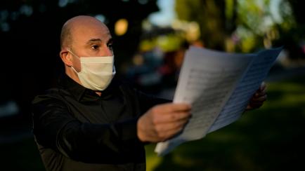 Member of chorus known as "Orfeon Pamplones'' wears a face mask protection against the coronavirus while singing a song in support for health public services as a tribute outside of Navarra Hospital, in Pamplona, northern Spain, Friday, May 29, ...