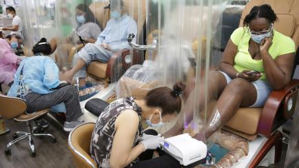 Candace Sanders, right, sits behind a plastic curtain while getting a pedicure at HT&V Nails in the Harlem section of New York, Monday, July 6, 2020. Nail salons and dog runs were back in business on Monday as New York City entered a new phase i...