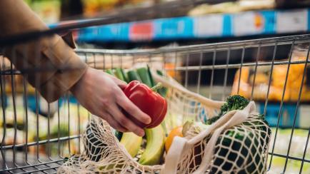 Una persona metiendo verduras en el carrito del supermercado.