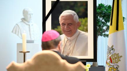Un obispo presenta sus respetos ante un retrato de Benedicto XVI en una iglesia alemana