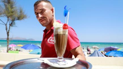 Un camarero sostiene una bandeja en una playa de Mallorca en agosto.