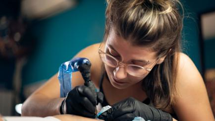 Focused female tattoo artist, tattooing the unrecognizable customer in her tattoo studio