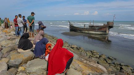 TOPSHOT - Villagers look at a wooden boat used by Rohingya people in Pidie, Aceh province on December 27, 2022. - Rohingya refugees received emergency medical treatment after a boat carrying nearly 200 people came ashore in Indonesia on December...
