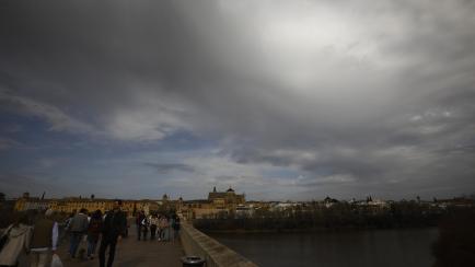 Varias personas caminan por el puente Romano de Córdoba con un sol tapado por la calima subida de temperaturas.
