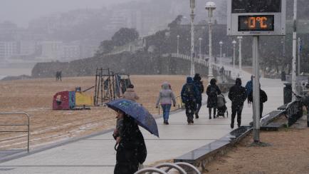 Varias personas caminan por el paseo marítimo de la playa de Ondarreta mientras nieva.