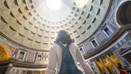 Una mujer observa como la luz entra por el techo del Panteón de Roma.