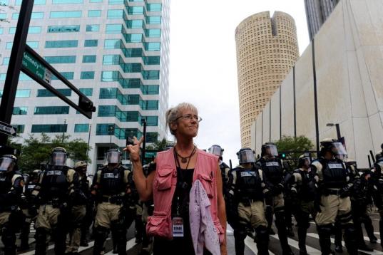 Una mujer hace el signo de la paz frente a un grupo de antidisturbios