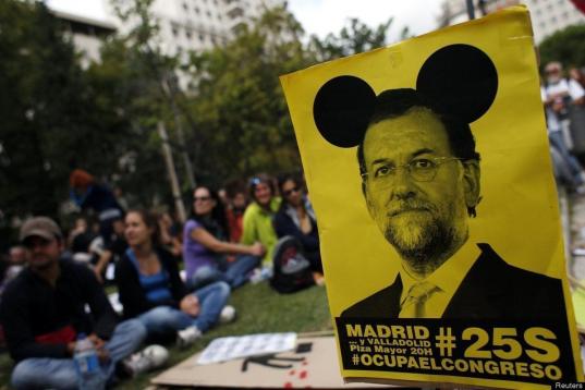 Un grupo de manifestantes esperan el inicio de la protesta, al lado un anuncio de la marcha con la imagen de Mariano Rajoy. 