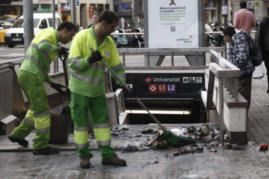  Operarios de limpieza retiran restos de un pequeño incendio en las puertas del metro Universitat, en Barcelona.