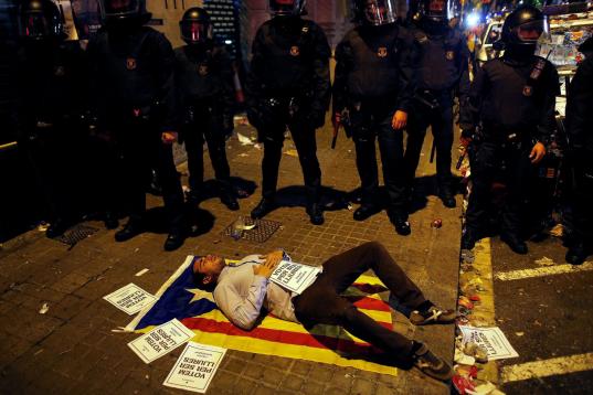 Un manifestante se tumba en una estelada junto a los Mossos d'Esquadra a las puertas de la Consellería de Economía en Barcelona en la madrugada del miércoles 20 de septiembre al jueves 21 de septiembre. 


