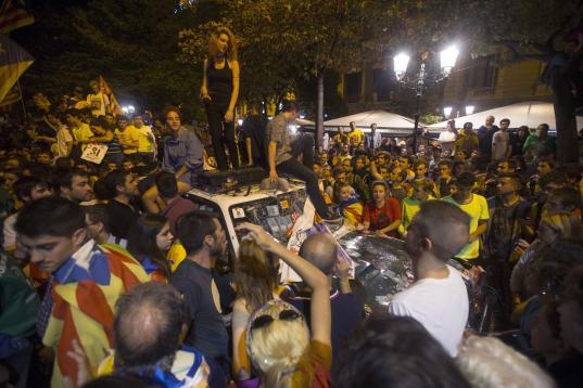Varios manifestantes se suben en los coches de la Guardia Civil mientras los agentes registran la Consellería de Economía en Barcelona. 


