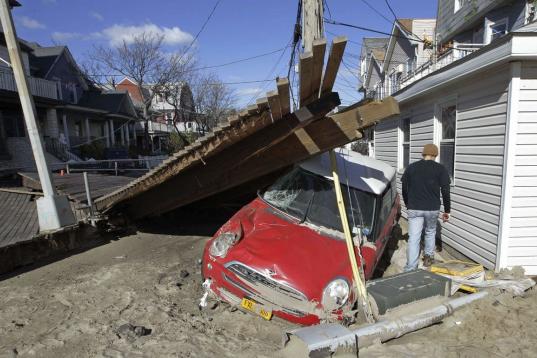 Foto del sábado 3 de noviembre del 2012 junto a un vehículo destrozado en el barrio neoyorquino de Rockaway por el huracán Sandy, que ha creado una carestía de automóviles de alquiler. (Foto AP/Kathy Willens)