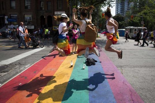 Tres mujeres saltan sobre un arcoíris pintado en el suelo en una calle de Toronto.