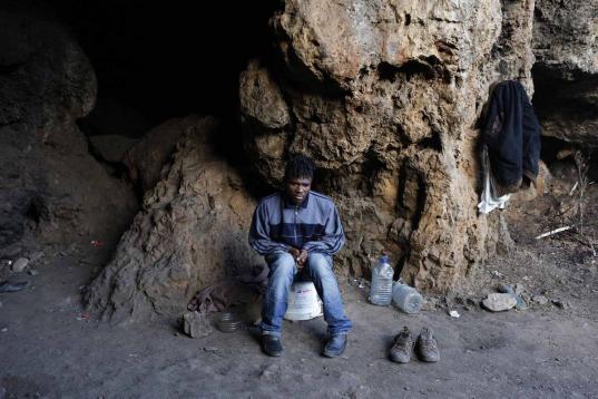 El camerunés Adria, sentado en su escondite de Ceuta junto a dos bidones de agua y un par de zapatos.