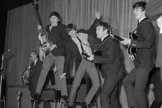 The Beatles jump on stage, left to right, Paul McCartney, Ringo Starr, John Lennon, and George Harrison.