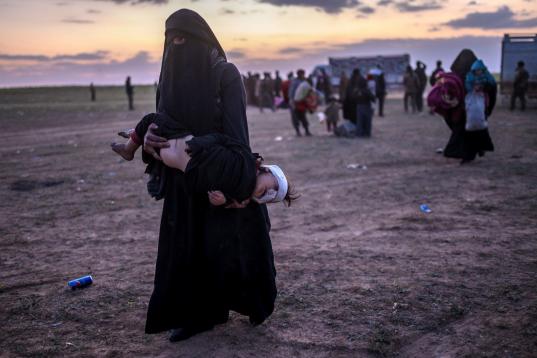 Una mujer completamente tapada, como impone el Estado Islámico, carga con un niño herido, tras escapar de Baghouz. 