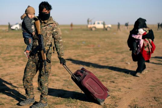 Un miembro de las milicias kurdas atiende a una mujer y a su bebé, recién escapados de Baghouz. 