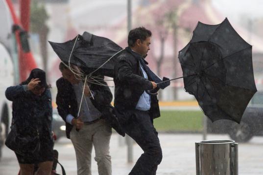 Varias personas sujetan sus paraguas intentando que no se les vuele debido al fuerte viento y a la lluvia en Málaga.