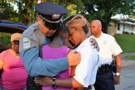 Los agentes de policía Greg Casem y Dominica Fuller consuelan a una niña en una vigilia en honor de Jamyla Bolden en Ferguson, Missouri (Estados Unidos), que murió en la cama el 19 de agosto después de que alguien disparara numerosas veces c...