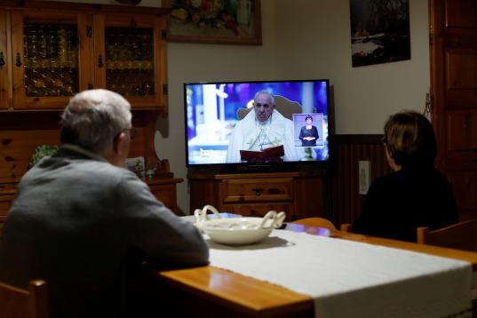 Un par de feligreses atienden a las palabras del papa por televisión