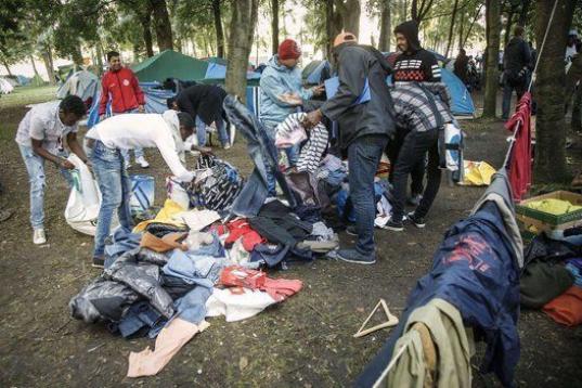 Inmigrantes se reparten la ropa que han donado para ellos en un parque cerca de la oficina de inmigración en Bruselas, el 2 de septiembre. 

