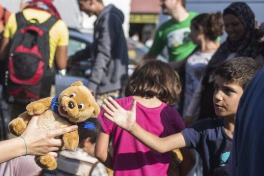 Una trabajadora de la iniciativa 'Ayuda a los Refugiados en Múnich' entrega un oso de peluche a un niño que espera con su familia un medio de transporte para acudir a uno de los centros de refugiados en la estación de Múnich (Alemania). 