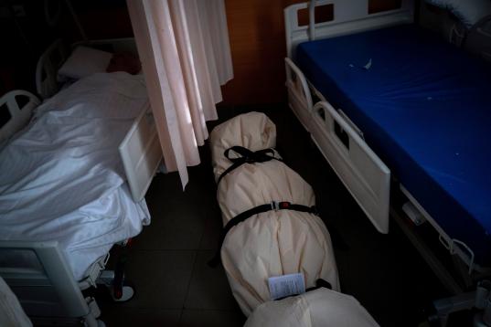 Una persona duerme en una cama a unos pocos pasos de un cadáver, envuelto en bolsas protectoras y tendido en el piso de un centro de mayores, en Barcelona, el 19 de noviembre de 2020.